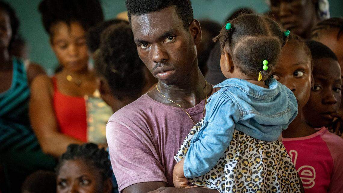 A man holding a child lines up to get medical attention at Ecole National Joseph C Bernard DeFreres Displacement Camp. Residents of areas in Port-au-Prince have been forced to take refuge in camps such as this rather than stay in gang occupied territory.