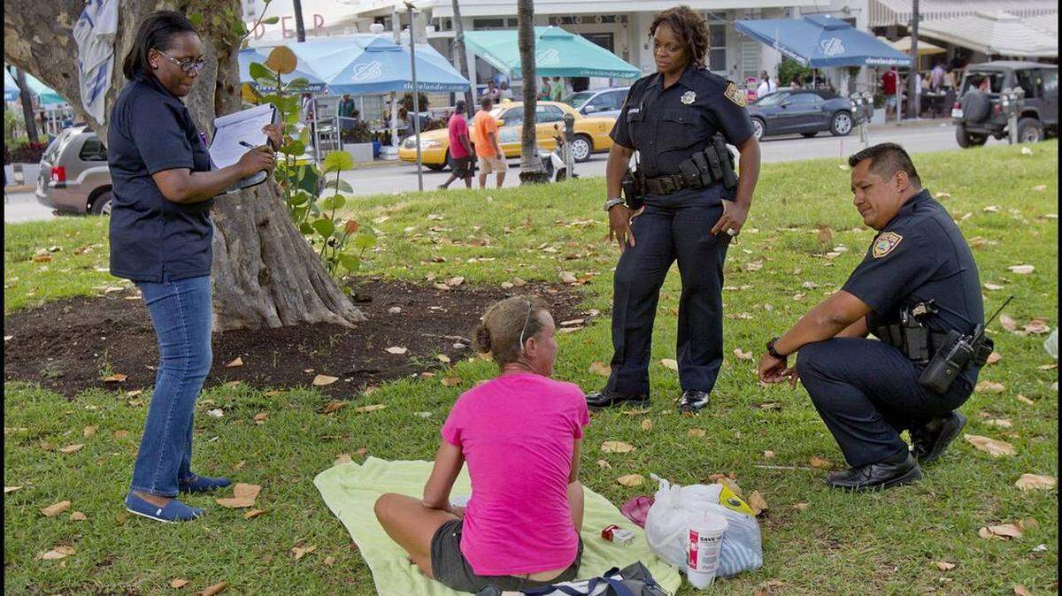 Miami Beach police officers talk with a homeless woman in Lummus Park in South Beach in June 2013.