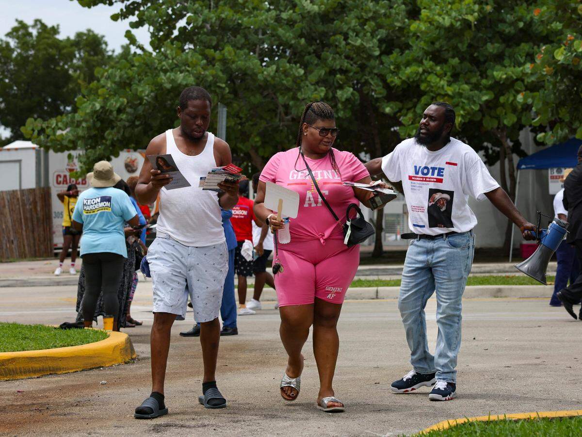 A campaigner stops two voters on their way in to vote during the last day of Early Voting on Sunday, Aug. 18, 2024, at the Jospeh Caleb Center in Miami. The poll worker said that this has been their busiest day of early voting.