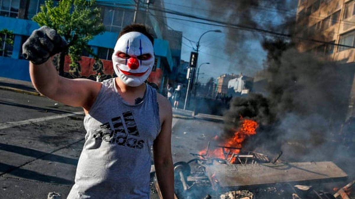 Masked demonstrator at a burning barricade in Valparaíso, Chile, during protesting a subway-fare increase.