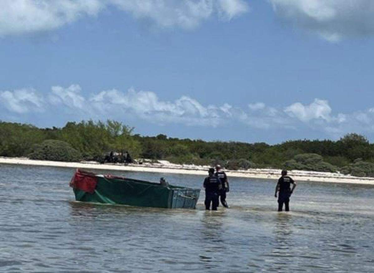 Federal agents stand near a boat in shallow water off a remote island about 20 miles west of Key West where 12 migrants from Cuba were found stranded Monday, June 13, 2022.