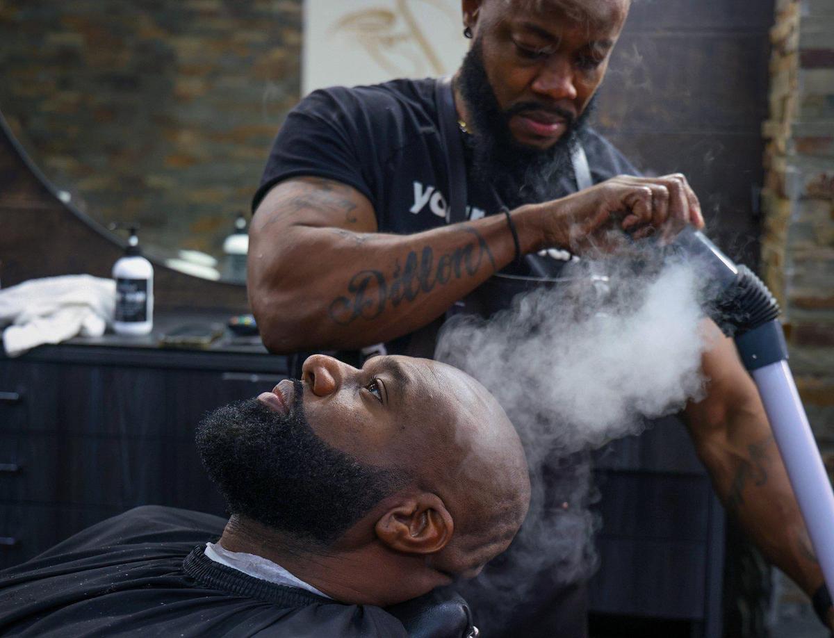 Barbershop owner Dwayne Dillion steams Rico Pradel’s shaved head after his beard was trimmed.