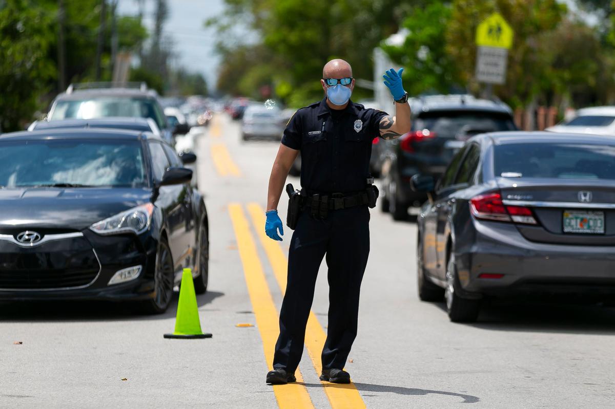 Police direct traffic as Miami-Dade County residents line up in their cars to receive a printed unemployment form at John F. Kennedy Library in Hialeah, Florida, on Tuesday, April 7, 2020.