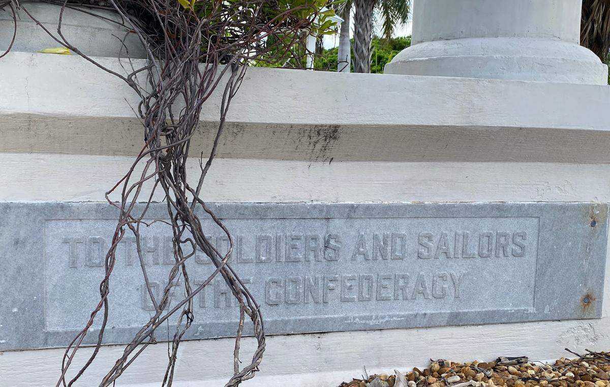 A plaque on the Confederate soldier memorial in Key West is partially blocked by a plant.