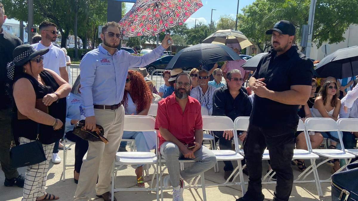 MIAMI HERALD FILE - Andy Santana, left in blue shirt, holds an umbrella over Alex Otaola at the commemoration of the 12th anniversary of Oswaldo Payá’s murder at the Patria y Vida Plaza at Walker Park in Hialeah, on Friday, May 10, 2024. Santana, the campaign manager of Otaloa, who was defeated in the August primary in his run for Miami-Dade mayor, was arrested on Thursday, Oct. 3, 2024, in his Hialeah home and charged with single counts of having sex with a minor and contributing to the delinquency of a minor.
