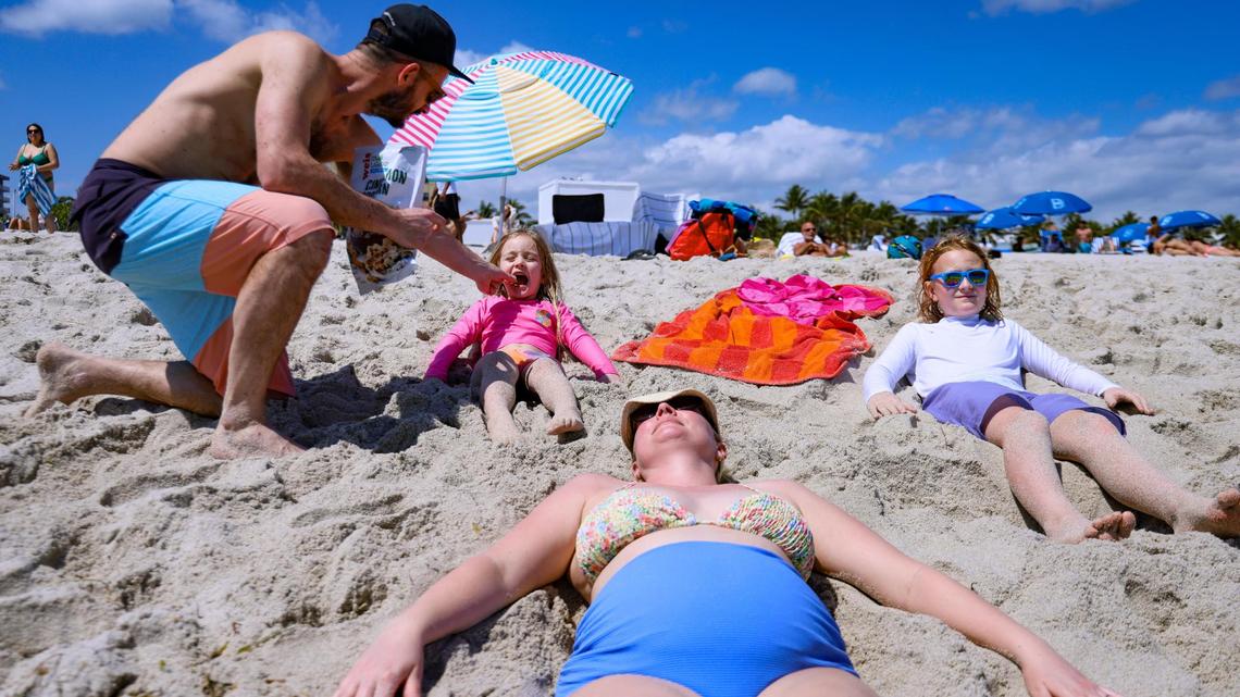 Tom Collins, left, feeds Elizabeth Carlisle, 5, as his wife Nancy Carlisle, and son, William Collins, enjoy a moment at South Beach while visiting from Pennsylvania for Spring Break in Miami Beach, Florida, on March 13, 2025.