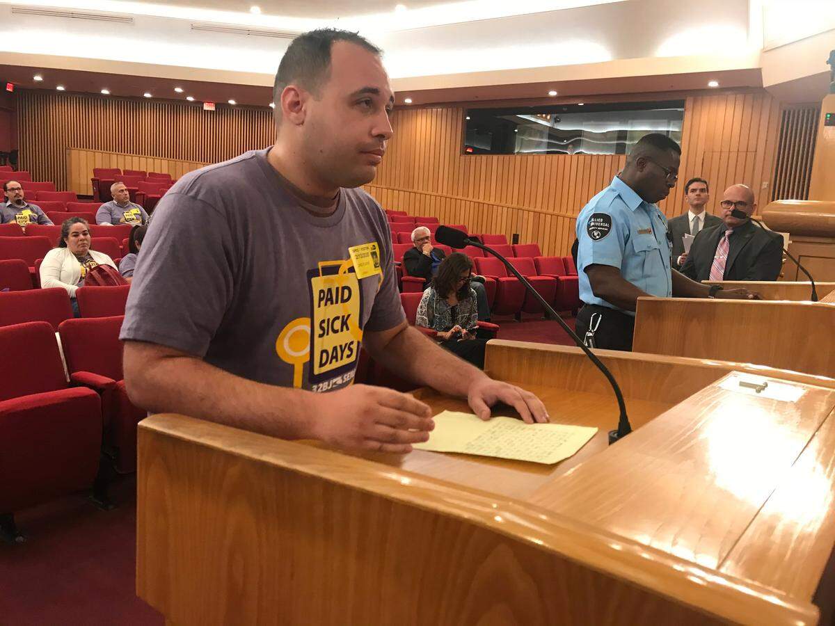 Joshua Lee Bleicher, a Metrorail guard, addresses Miami-Dade commissioners on Thursday, Feb. 13, 2020, about a bill that would require county contractors to provide workers like him paid sick time, family leave and parental leave. At the other lectern, airport guard Roosvelt Derameau waits his turn to speak.