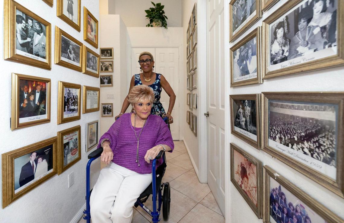 Caregiver Avis Walker gives aide to Connie Francis, a popular American pop singer of the late 1950s and early 1960s, as Francis looks over a hallway filled with framed photographs of her with celebrities and displayed at her home in Parkland, Florida on Friday, June 6, 2025.