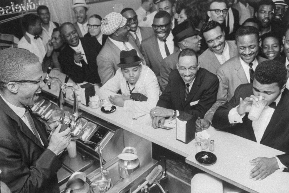 MIAMI - February 1964: Black Muslim leader Malcolm X (L), behind soda fountain, joking with tux-clad Cassius Clay (now Muhammad Ali)(R), who responds with mock indignation while surrounded by jubilant fans after he beat Sonny Liston for the heavyweight championship of the world. (Photo by Bob Gomel/The LIFE Images Collection via Getty Images/Getty Images)