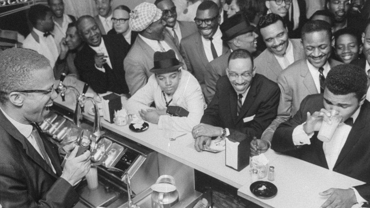 MIAMI - February 1964: Black Muslim leader Malcolm X (L), behind soda fountain, joking with tux-clad Cassius Clay (now Muhammad Ali)(R), who responds with mock indignation while surrounded by jubilant fans after he beat Sonny Liston for the heavyweight championship of the world. (Photo by Bob Gomel/The LIFE Images Collection via Getty Images/Getty Images)