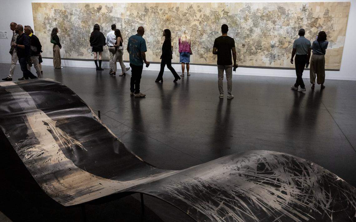 People make their way past “Amazogramas” by Roberto Huarcaya, below, and “Untitled” by Antonis Donef, above, on display during Art Basel at the Miami Beach Convention Center on Saturday, Dec. 7, 2024, in Miami Beach, Fla.