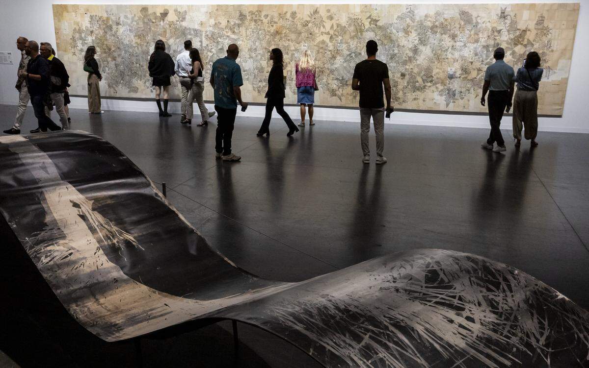 People make their way past “Amazogramas” by Roberto Huarcaya, below, and “Untitled” by Antonis Donef, above, on display during Art Basel at the Miami Beach Convention Center on Saturday, Dec. 7, 2024, in Miami Beach, Fla.