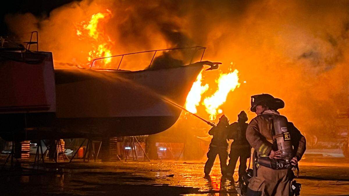 Monroe County Fire Rescue firefighters spray down a large boat engulfed in flames at Robbie’s Marina in Key West Monday night, July 22, 2024.