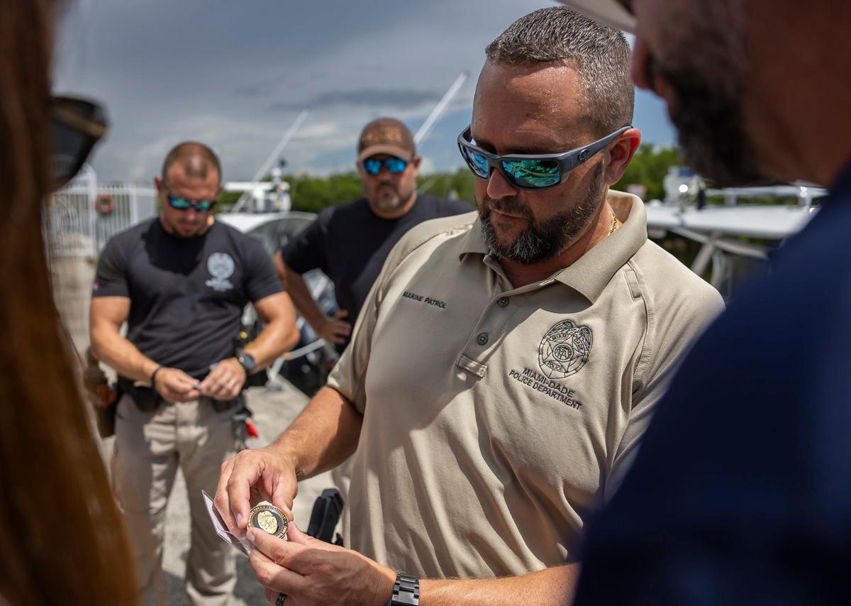Miami-Dade Police Lt. Michael Barrios presents Melissa and Andres Fernandez with a Marine Patrol Unit coin after hanging Fly High, Bird flags on their patrol boats at the Black Point Park and Marina on Friday, Aug. 30, 2024, in Homestead, Fla.