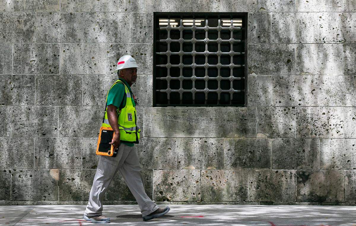 A construction worker walks on Flagler Street past a grated window on the fortress-like base of the Miami-Dade Cultural Center in downtown Miami.