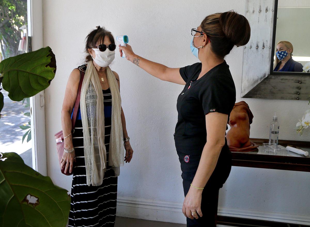 Nail specialist Niurca Hernandez Labori takes the temperature of client, Olga Leiseca, as she arrives for her appointment at Body & Soul Salon & Med Spa, which implemented a strict procedure for costumers and employees as the City of Miami cautiously authorized the reopening of non-essential businesses.