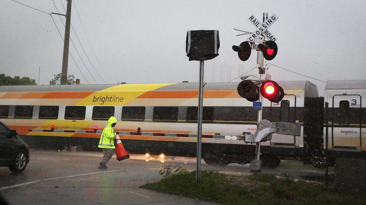 A crossing guard, employed for extra safety at the railroad tracks when Brightline trains cross intersections. runs to move a traffic cone out of the street at the intersection of Northeast 20th St. and North Miami Avenue in this June 4, 2018 file photo. The guards place the cones in the roads as the high-speed trains pass to keep cars at a safe distance from the tracks.