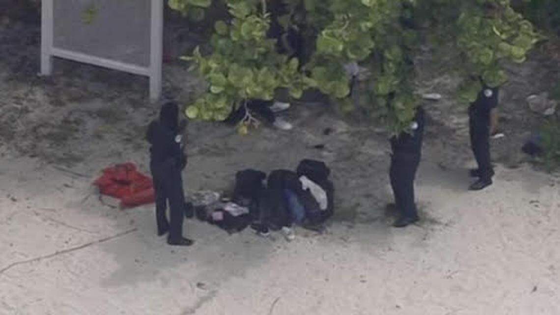 Federal agents stand by a group of people sitting on Sunny Isles Beach Monday, May 15, 2023, who the Border Patrol said are migrants from China.
