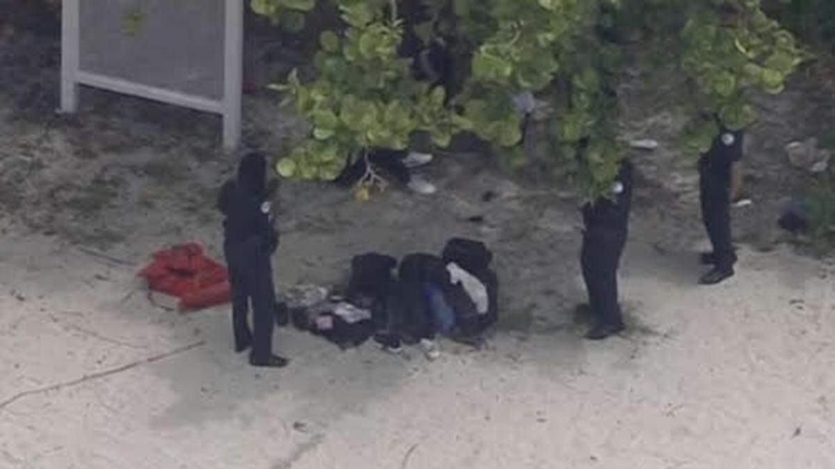 Federal agents stand by a group of people sitting on Sunny Isles Beach Monday, May 15, 2023, who the Border Patrol said are migrants from China.