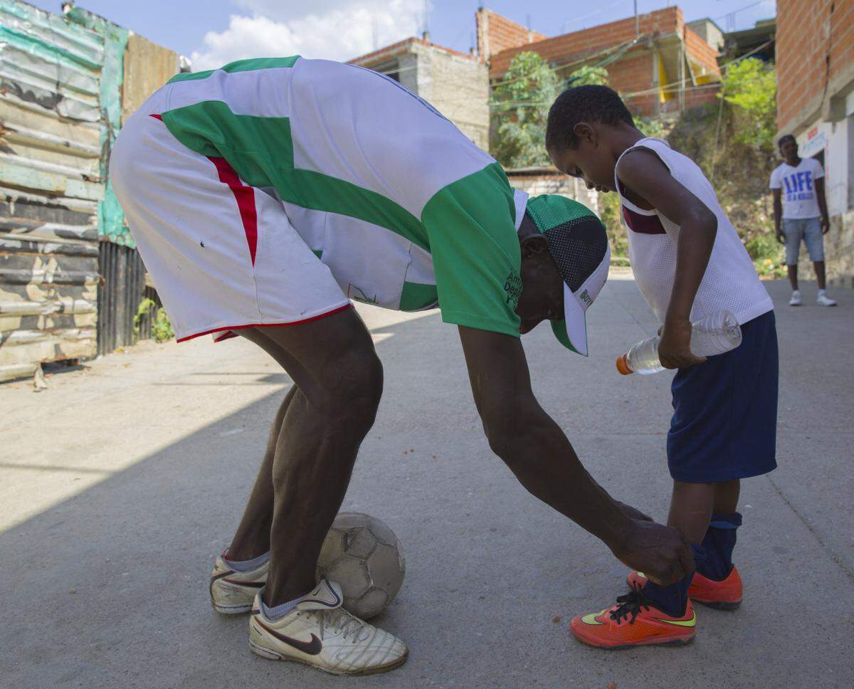 Trainer Iván Torres helps 6-year-old Isaac Canoles lace up the soccer shoes he received from the NGO Pasión Petare. The hope is to get enough donations to help the children participate in tournaments with equal equipment.