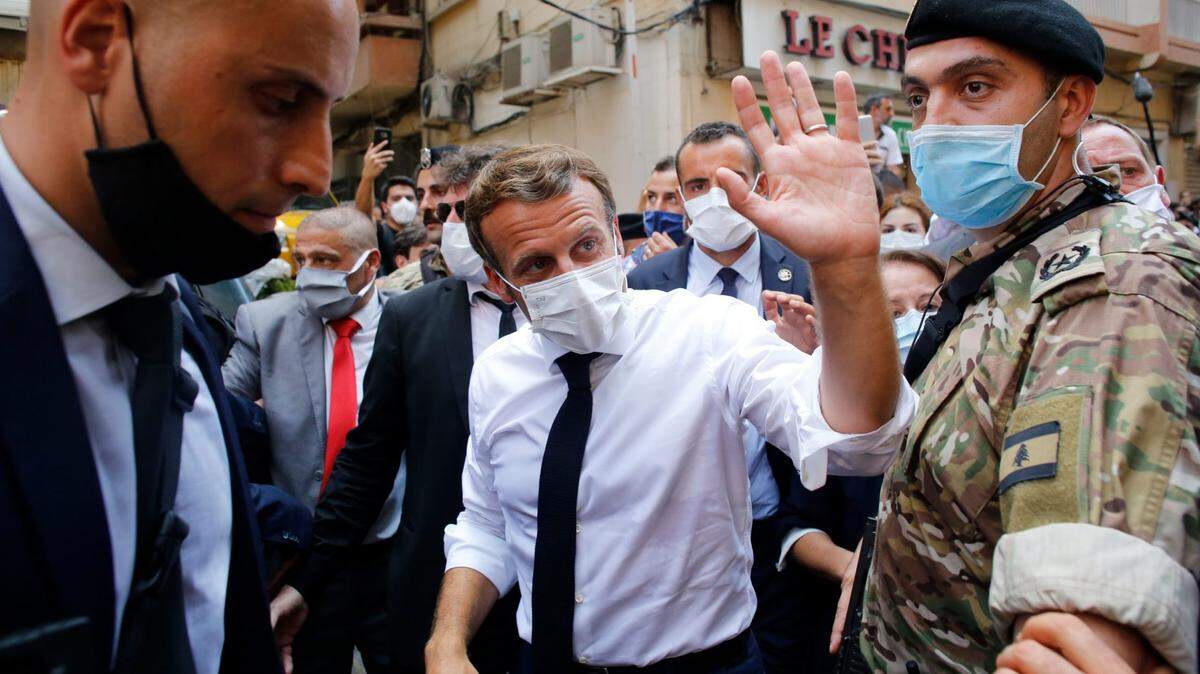 French President Emmanuel Macron waves as he walks a devastated street of Beirut, two days after a massive explosion devastated the Lebanese capital in August.