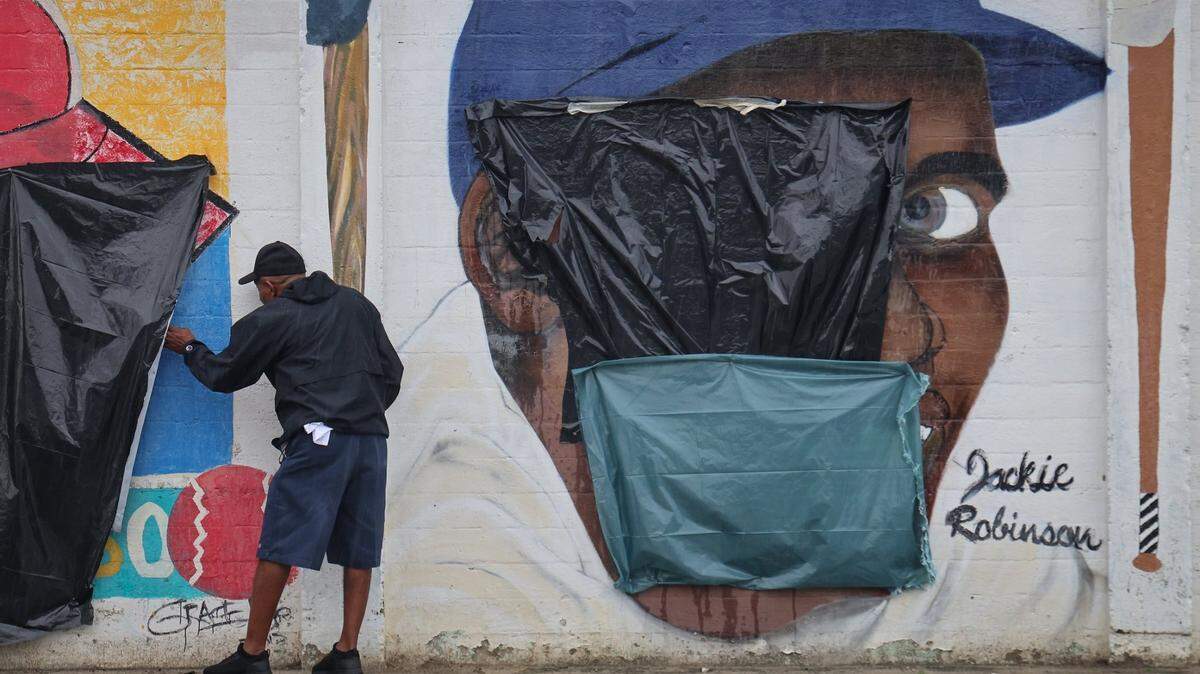 An unidentified employee of the Downtown Development Authority takes a peek of a mural of Minnie Miñoso behind the plastic that covers a swastika. Next to it is a mural of Jackie Robinson. The murals were defaced with a swastika and Jim-Crow era racial epithet at Overtown’s Dorsey Park, Tuesday, June 3, 2025.
