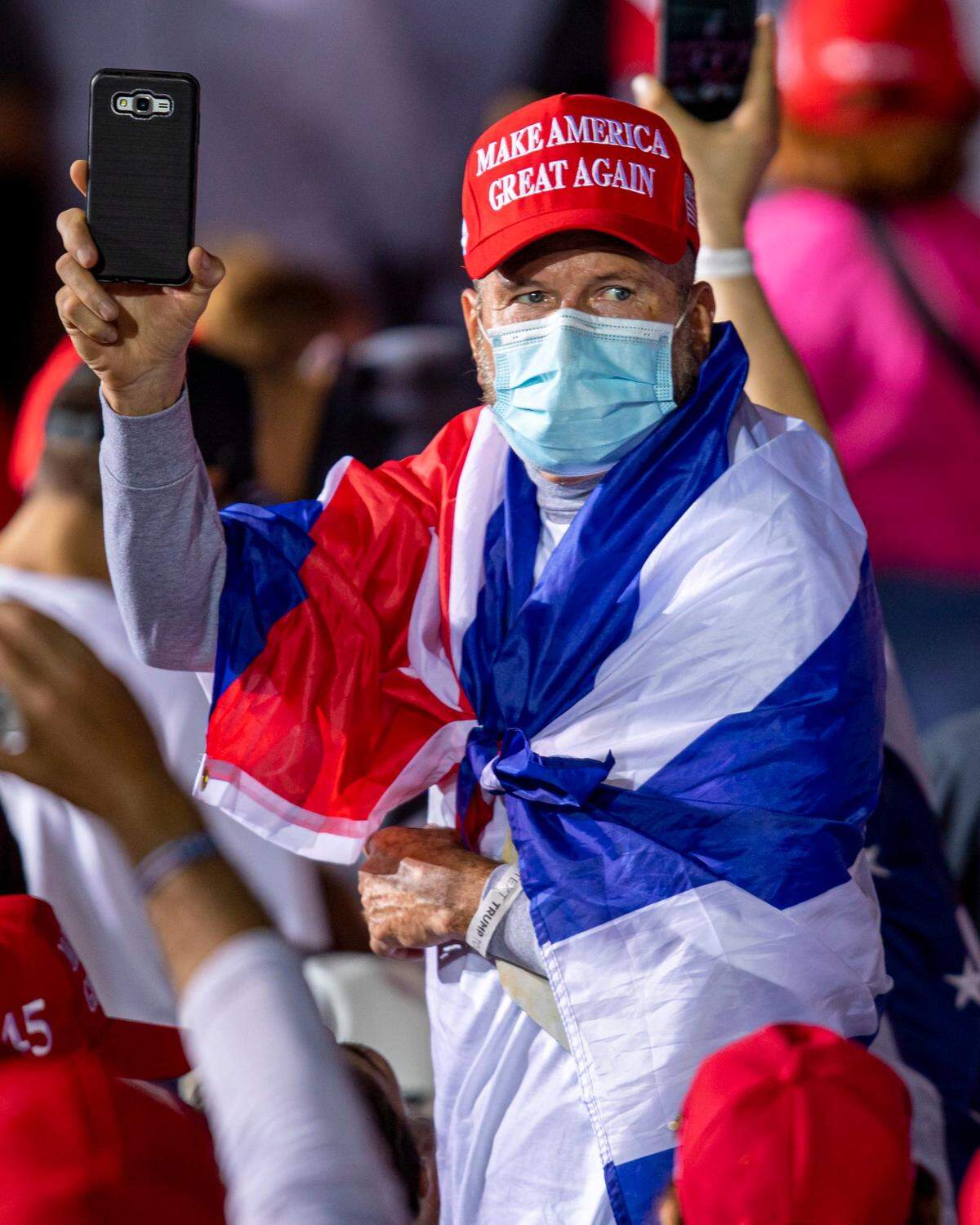 Un partidario de Trump envuelto en una bandera cubana mira hacia la multitud durante el Mitin de Victoria Make America Great Again, en Signature Flight Support OPF - Aeropuerto Ejecutivo Opa-Locka en Opa-locka, Florida, el domingo 1 de noviembre de 2020.