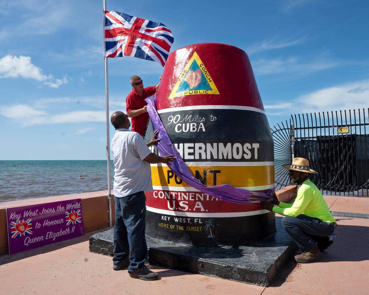 Personal de Servicios Comunitarios de Cayo Hueso colocan una banda púrpura alrededor del marcador del punto más al sur de Estados Unidos  en homenaje a la reina Isabel II, el viernes 16 de septiembre de 2022, en Cayo Hueso. La reina y el príncipe Felipe visitaron los Cayos el 18 de mayo de 1991 y recorrieron el histórico Fuerte Jefferson en las Dry Tortugas. De izquierda a derecha, Trent Richardson, Paul Cassidy y Christopher Coleman.