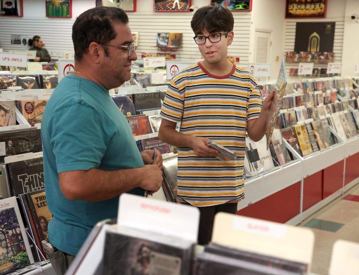 Eli Ramos, 50, left, and his son, Alessandro Ramos, 16, discuss their album selections while shopping at Museo del Disco in Miami-Dade County. Father and son are avid vinyl collectors.