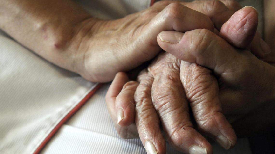 A nurse holds the hand of an elderly Alzheimer’s patient.