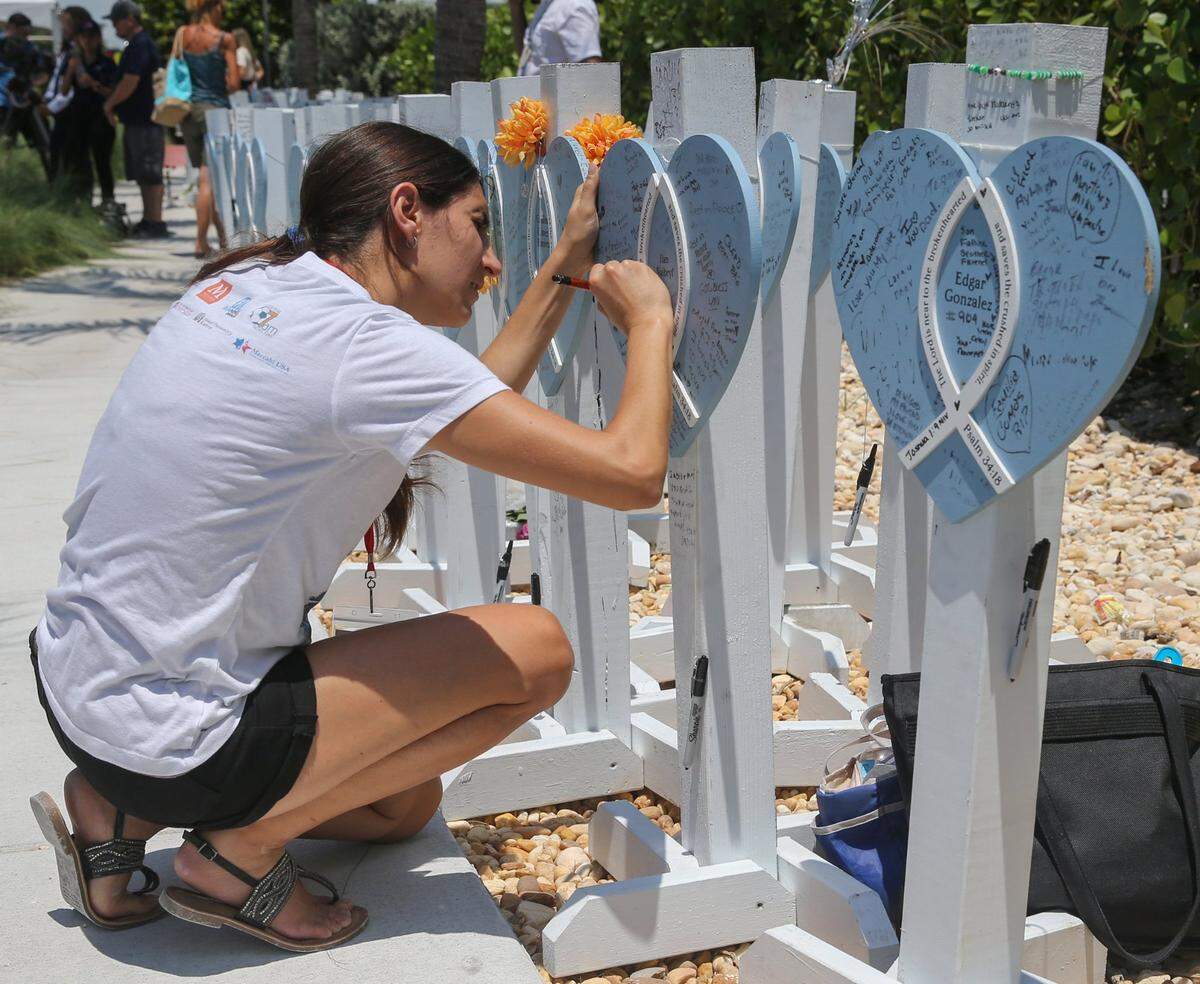 Dalia Gutman writes on a memorial marker for her cousin Ilan Naibryf during a public memorial event to mark the one-year anniversary on Friday, June 24, 2022, of the collapse of Champlain Towers South in Surfside, Florida.