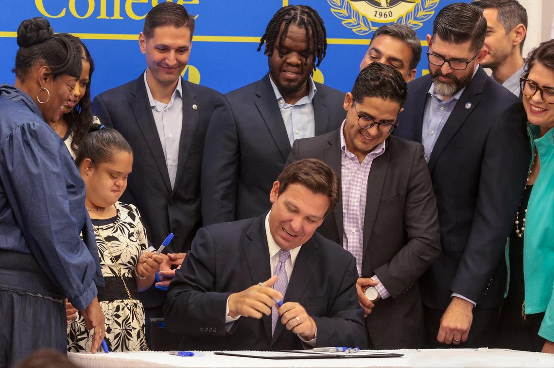 On Tuesday, April 12, 2022, Gov. Ron DeSantis, center, signs a bill that financially benefits more people who care for needy children and helps additional children who were in the foster care system attend a state college or university. The bill signing took place at Miami Dade College Wolfson Campus in Miami, Florida.