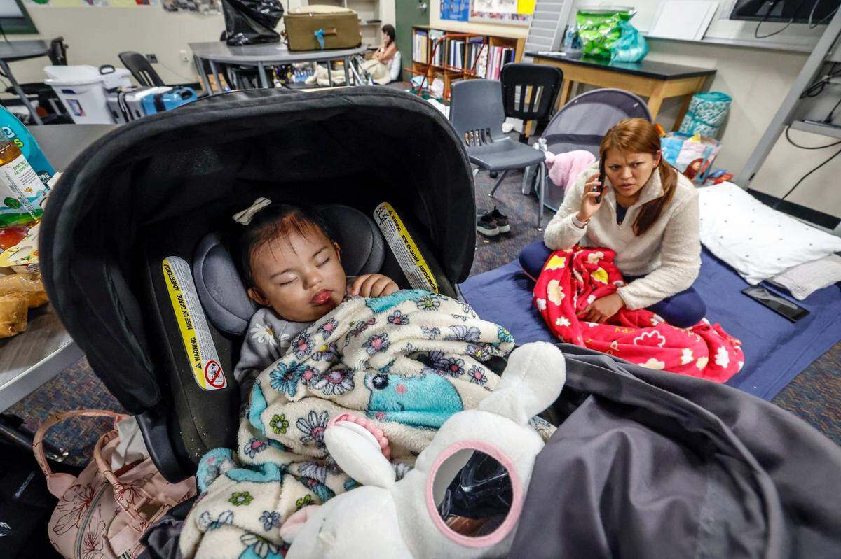 Evacuee Maria Lavy speaks on the phone as her baby Melanie Lavy 1, sleeps at hurricane shelter in Brookside Middle School in Sarasota, Florida on Wednesday, October 9, 2024.
