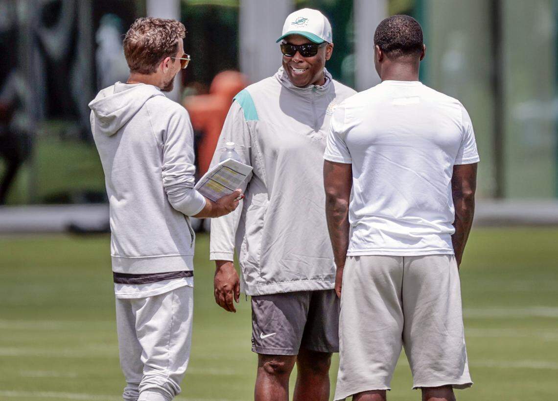 Miami Dolphins head coach Mike McDaniel speaks with general manager Chris Greer and running back De'Von Achane (28), left to right, during practice at the Miami Dolphins Training Camp in Miami Gardens, Florida, on Wednesday, August 27, 2025.