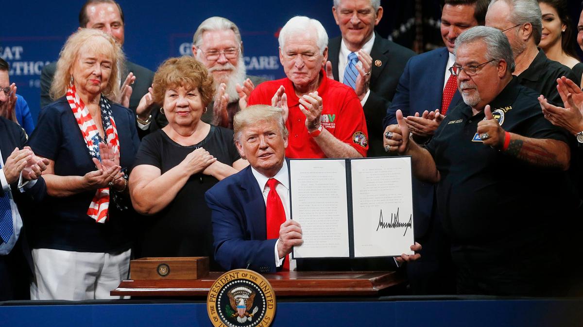 President Donald Trump signs an executive order on Medicare while his supporters look on, including Florida Gov. Ron DeSantis, at the Sharon L. Morse Performing Arts Center in The Villages, Florida, on Thursday, Oct. 3, 2019.
