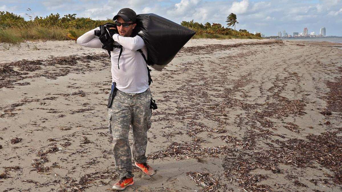 In 2019, Andrew Otazo removes a bag full of trash from the mangroves and coral reef at Bear Cut during low tide.