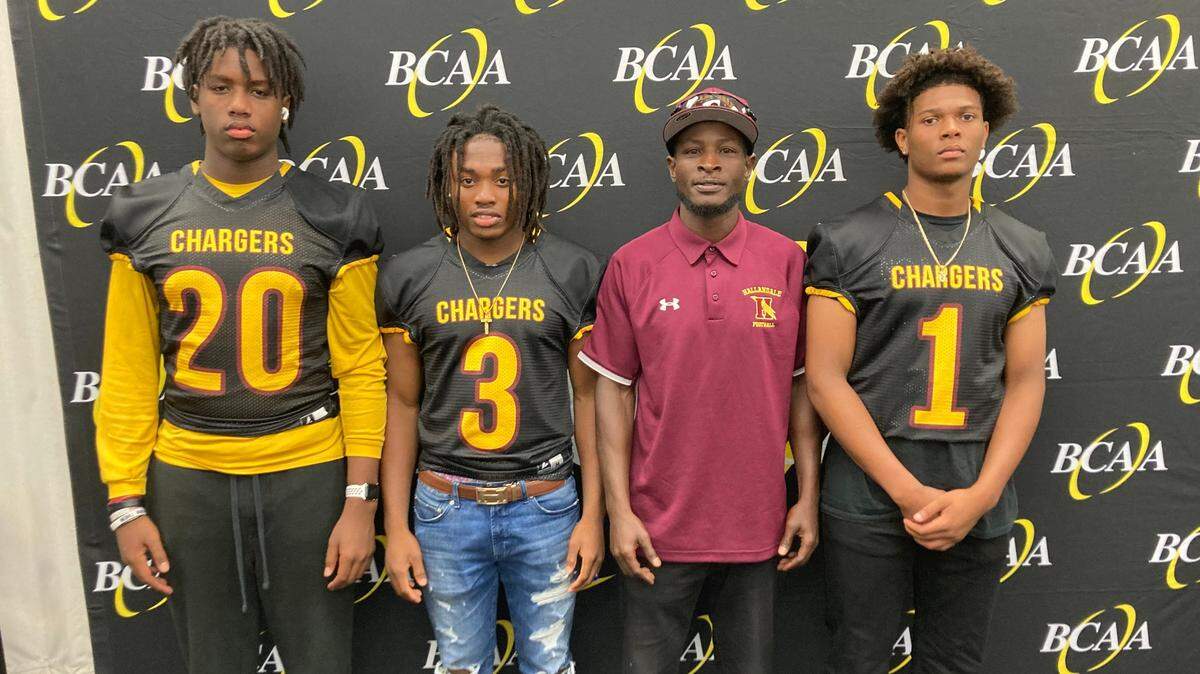 Hallandale High football coach Joshua Bush and players Javari Johnson (20), Raynaldo Narcisse (3) and Michael Bradley (1) represented their school at the recent Varsity Sports Network High School Football Media Day in Pompano Beach. The Chargers, once a playoff regular, are looking to rebuild from a winless season in 2021.