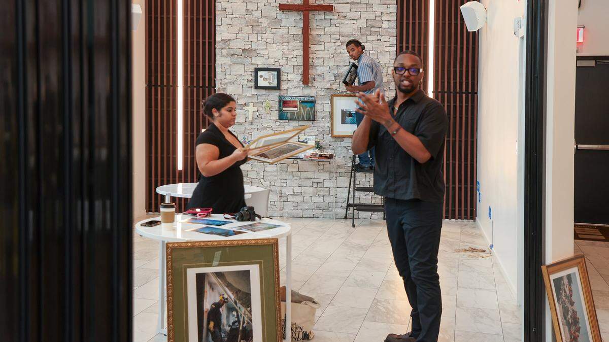 Curator Alford Archer, 15, looks back prior to installing art work on the wall as Hannah Cabrera, 17, left, and Nyya Toussaint continue the installation of artwork. Four high school students installed photos inside the First Church Miami coffee shop for the exhibition Sparrow, featuring the photography of local photographers navigating homelessness under the artistic direction of Miami-based artist Christopher Mitchell on Sunday, November 30, 2025.