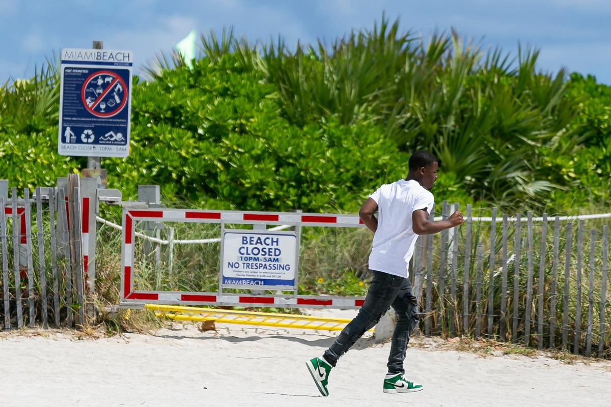 A man walks past a closed beach entrance near Ocean Drive in Miami Beach, Florida on Saturday, March 14, 2020. To limit large crowds and fight the spread of COVID-19, Miami Beach officials are closing three blocks of the public beach on South Beach beginning Saturday and lasting indefinitely.