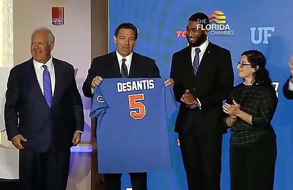 In this framegrab from video, Gov. Ron DeSantis accepts a baseball jersey from University of Florida Board of Trustees Chairperson Mori Hosseini, left, when UF tied for fifth nationally in the annual ranking of public universities by U.S. News and World Report.