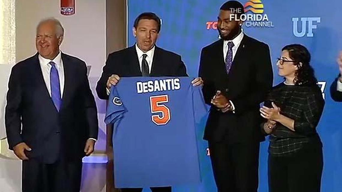 In this framegrab from video, Gov. Ron DeSantis accepts a baseball jersey from University of Florida Board of Trustees Chairperson Mori Hosseini, left, when UF tied for fifth nationally in the annual ranking of public universities by U.S. News and World Report.