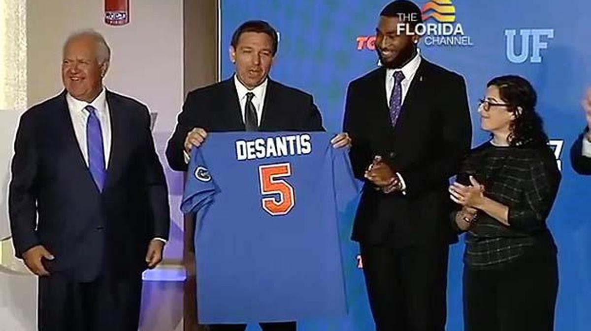 In this framegrab from video, Gov. Ron DeSantis accepts a baseball jersey from University of Florida Board of Trustees Chairperson Mori Hosseini, left, when UF tied for fifth nationally in the annual ranking of public universities by U.S. News and World Report.