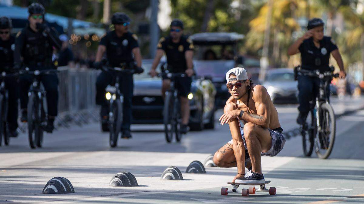 A skater makes his way down Ocean Drive as police patrol the street on Friday, March 24, 2023 in Miami Beach, Fla. After two deadly shootings, city officials voted not to re-impose a midnight curfew, but implemented an emergency order banning alcohol sales after 6 p.m.