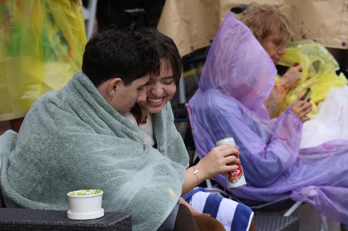 Sal Perrone, left, 24, a chemist, and his girlfriend Juliana Bach, 23, enjoy each other company as they wait for the start of the parade. It was singing, dancing, and parading in the rain as Coconut Grove held its annual satirical parade on Sunday, January 7, 2023 in Miami, Florida.