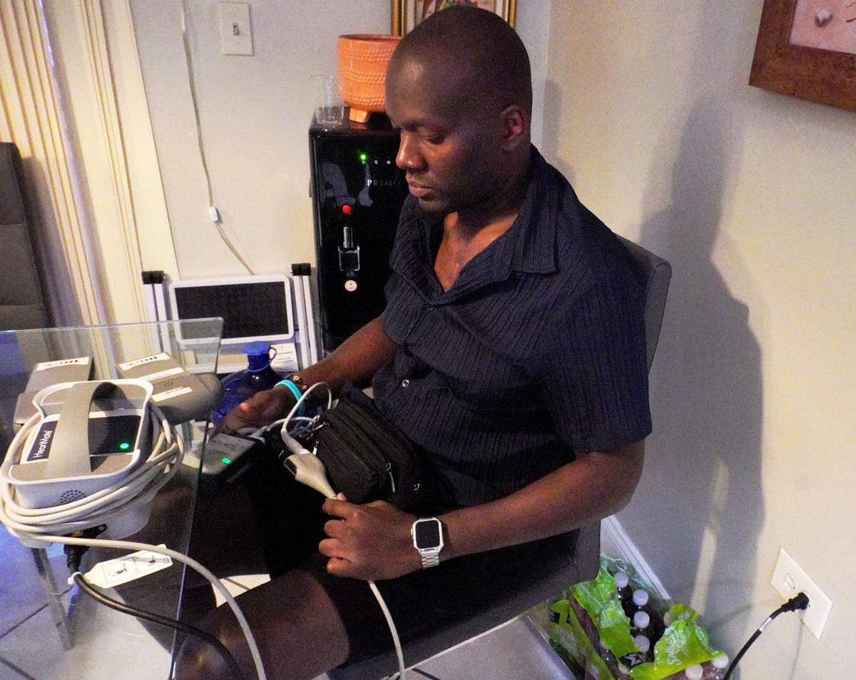 Claude Jn Baptiste, who must wear his left ventricular assist device 24/7, disconnects the batteries and plugs the device into an outlet. 