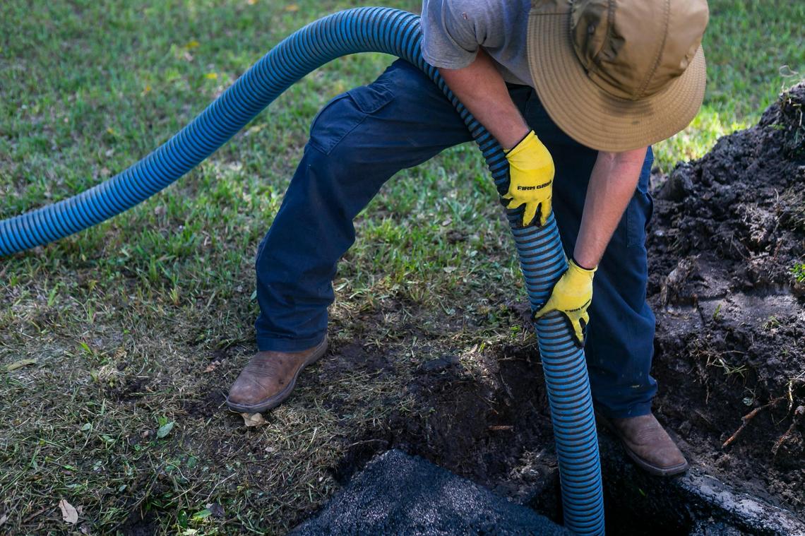 Jeremy Langford, an employee at AA ARON Super Rooter, center, cleans out a septic tank at a home in Miami, Florida on Wednesday, September 30, 2020.