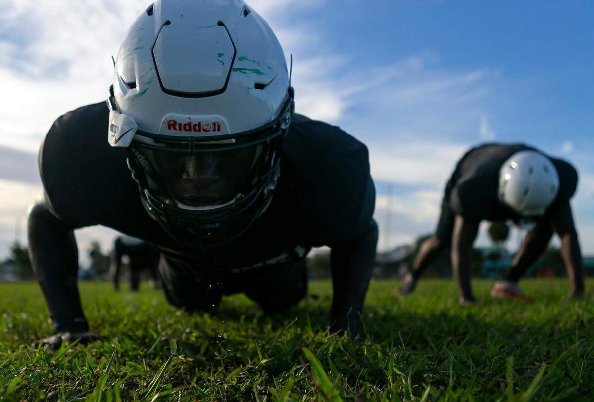 Miami Central football players do pushups during a preseason practice at their school’s field in Miami’s West Little River neighborhood on Thursday, August 5, 2021.