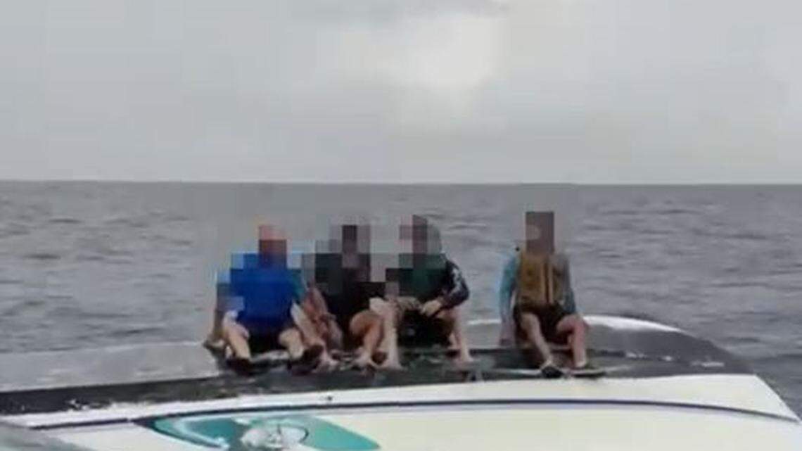 Four people sit on the bottom of an overturned boat about seven miles off shore of Haulover Inlet Sunday, Aug. 30, 2025.