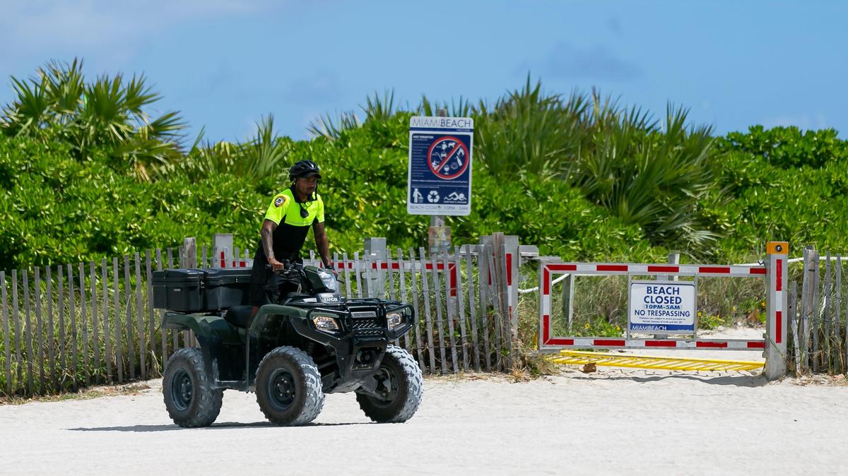 A police officer drives past a closed beach entrance near Ocean Drive in Miami Beach on Saturday, March 14, 2020. To limit large crowds and fight the spread of COVID-19, Miami Beach officials are closing three blocks of the public beach on South Beach beginning Saturday.