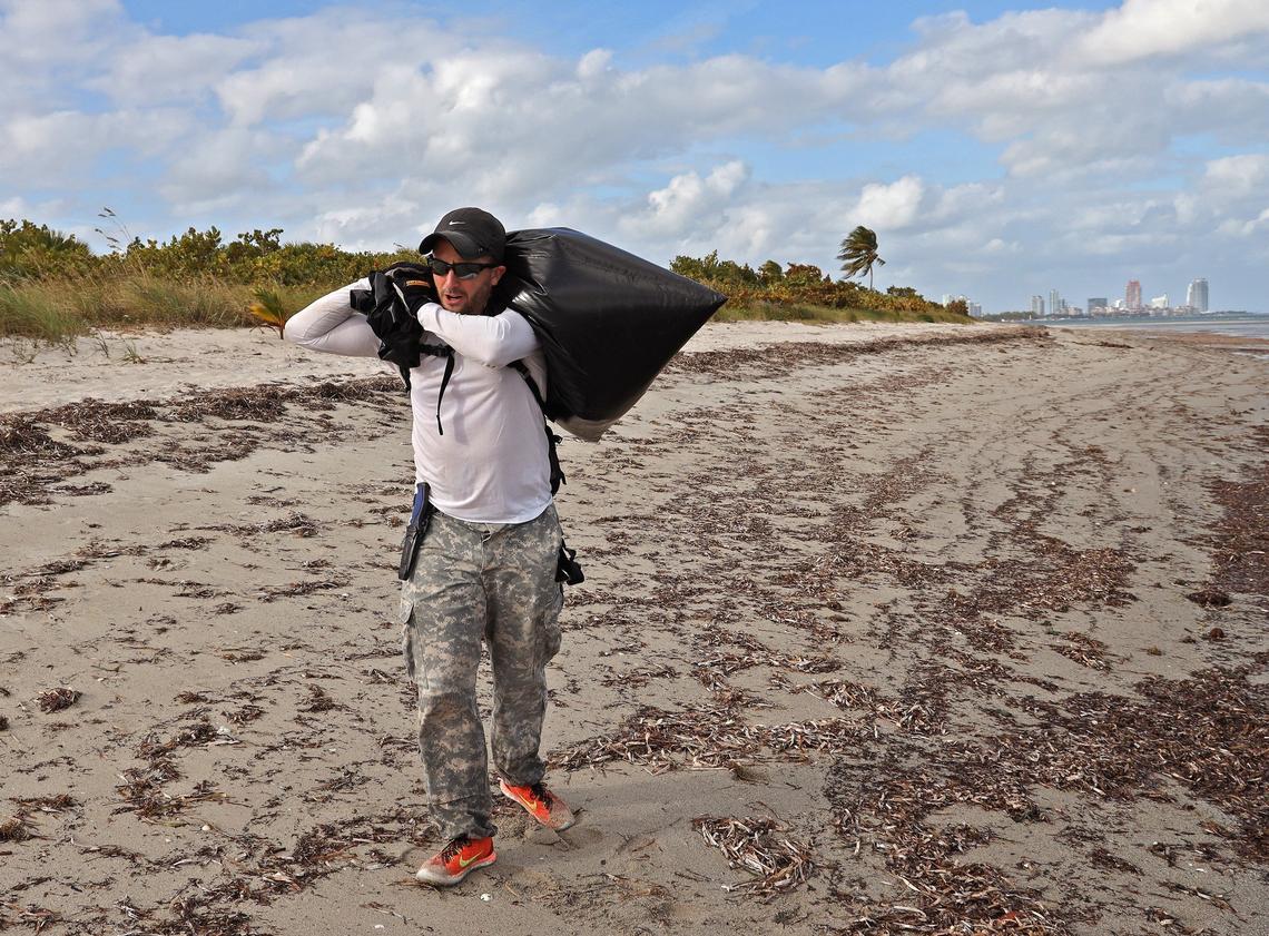 Andrew Otazo returns to his car after removing a bag full of discarded items from the mangroves and coral reef at Bear Cut during low tide.